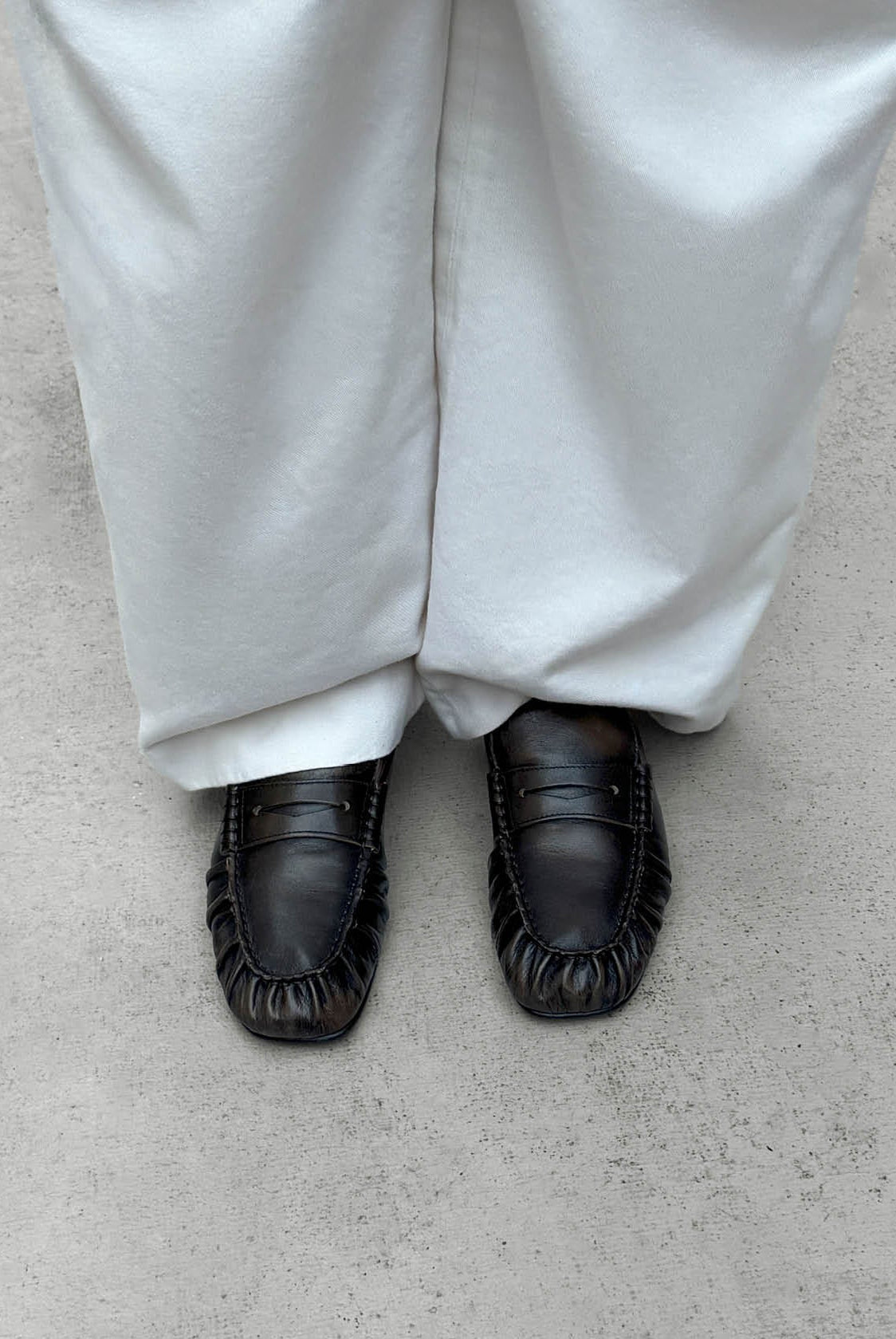 Alohas gathered leather penny loafers under the hem of pale grey wide leg trousers