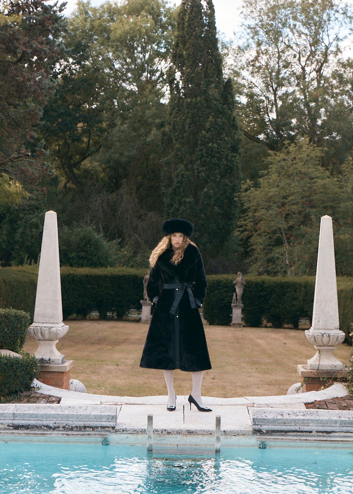 Queens of Archive Worn with a black fur hat and heels between stone obelisks, belted with a bow at the waist
