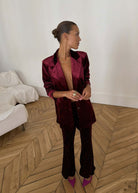 Standing pose with hands clasped, flared velvet trousers breaking over magenta heels