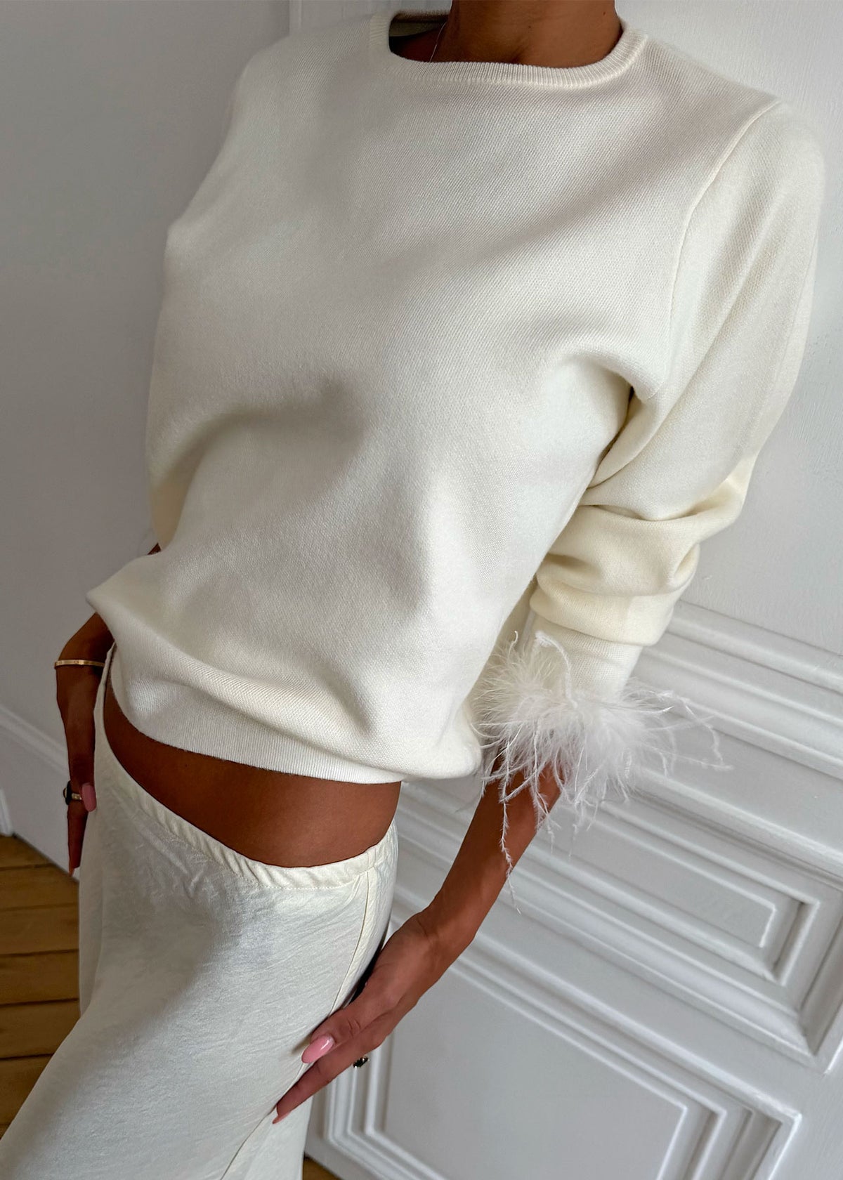 Never Fully Dressed Cropped fit with feather cuff, leaning against a panelled door