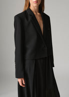 Deep notch lapel and leather-trimmed chest pocket, worn open over a pleated black midi skirt