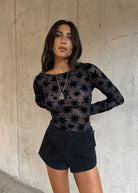 Styled with black suede shorts and layered gold necklace against concrete