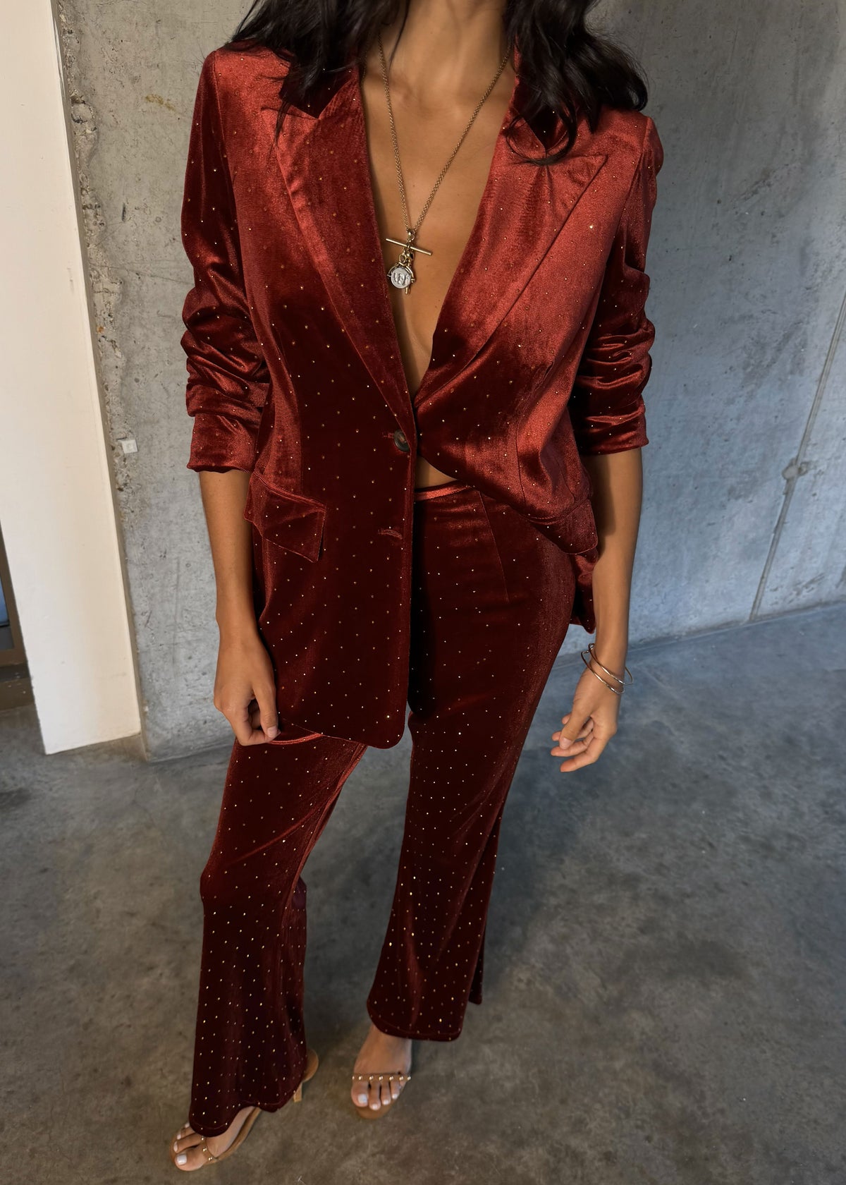 Never Fully Dressed Rust red colourway of the velvet trousers on concrete with clear strappy sandals
