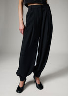 Close view of the pleated waistband and full leg gathering into a buttoned ankle cuff