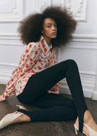 Seated styling shot worn untucked over black stirrup leggings and ivory slingbacks
