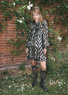 Worn with black lace knee socks and buckled flats, metallic floral print in cream and gold against brick