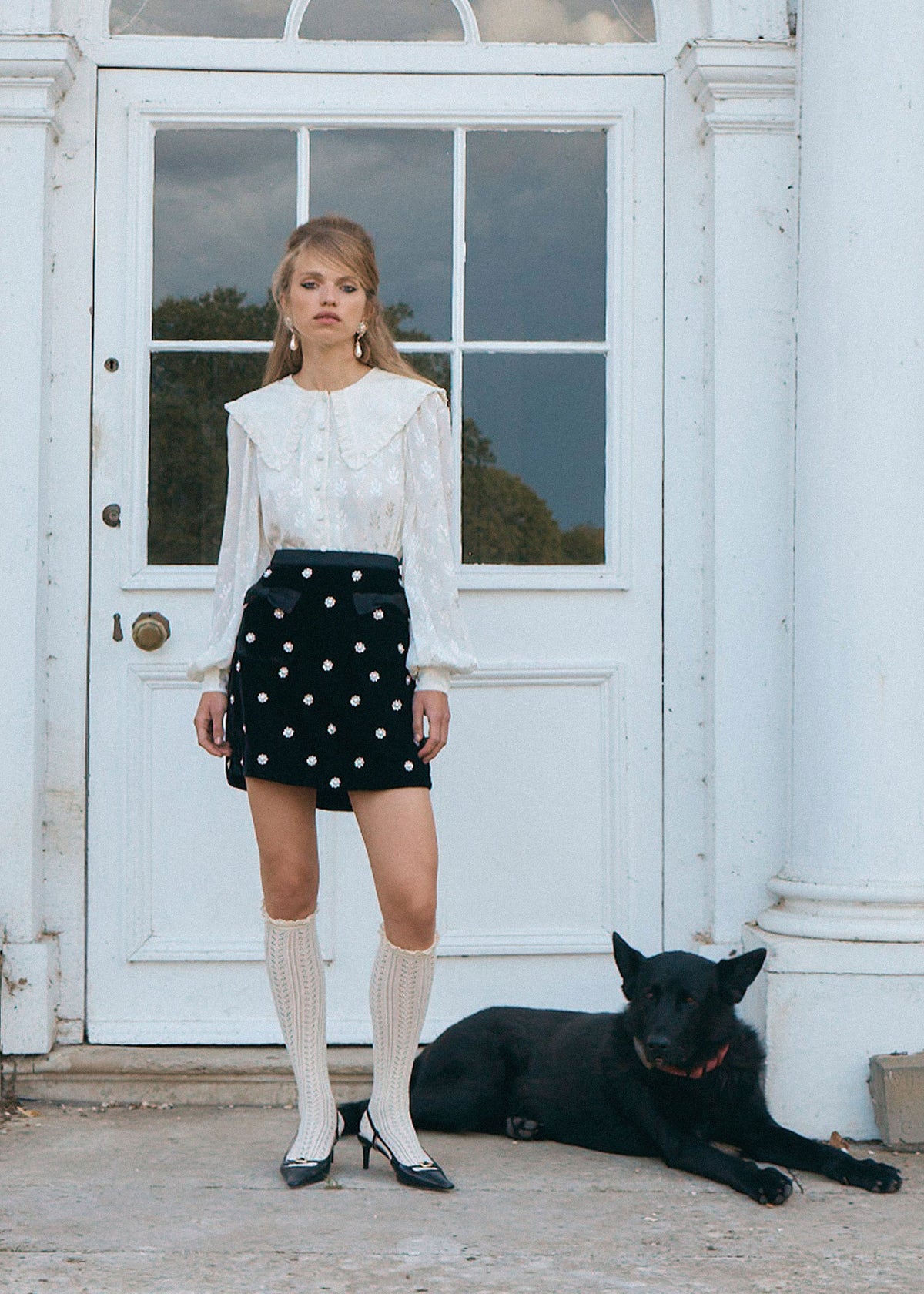 Queens of Archive Standing at a white doorway in slingback heels, collar and balloon sleeves over the velvet skirt