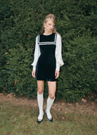 Styled with cream openwork knee socks and black strap shoes, in front of a clipped hedge