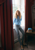 Standing at a sash window beside red curtains, buttoned over grey leggings
