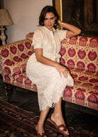 Seated on a patterned ikat chaise, broderie texture catching the light