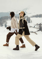 Walking across a snowy hillside, worn with wide-leg trousers and shearling layers