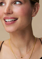 Worn layered over a flat snake chain, with pearl drop earrings and stacked studs