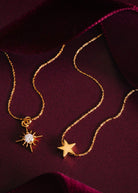 Flat-lay on burgundy satin, alongside a crystal starburst pendant on matching chain